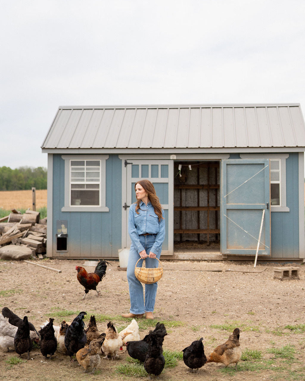 Woman standing in front of a small building with chickens around her