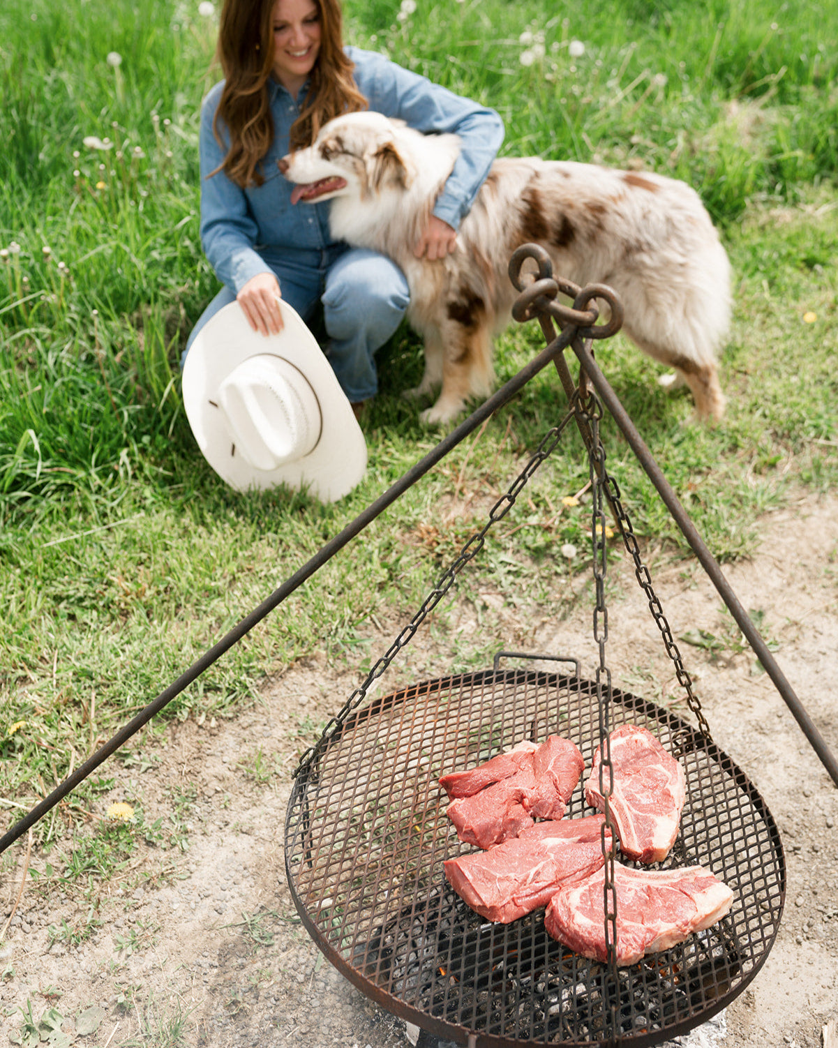 Woman with a dog and a grill with raw meat on a grassy outdoor setting